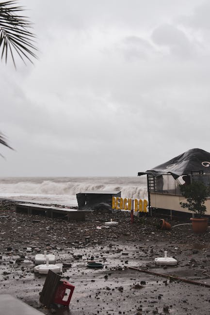 A coastal beach bar damaged by a recent storm with high waves, debris, and cloudy skies.